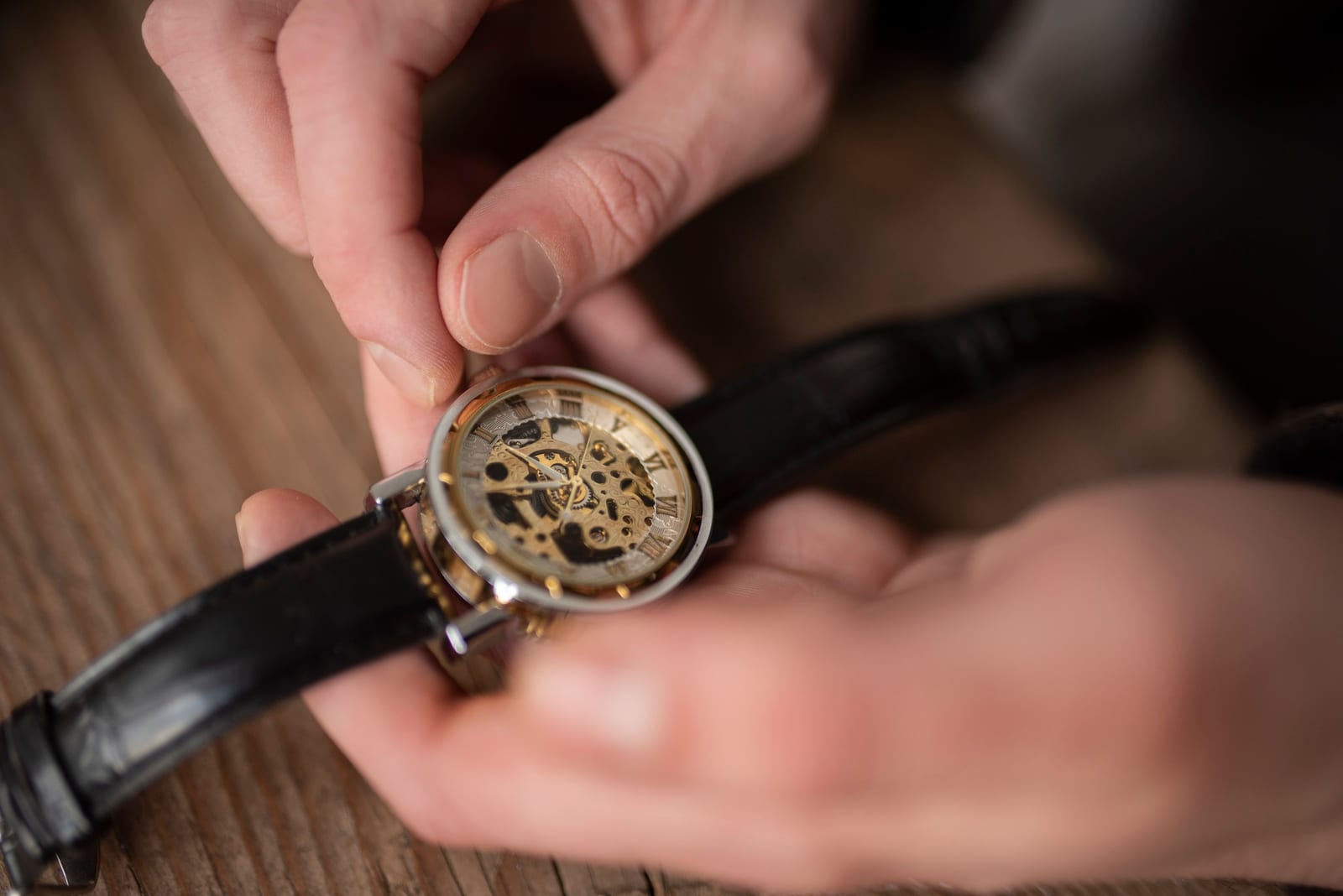 Mano che regola la corona di un orologio meccanico scheletrato indossato al polso, con cinturino nero