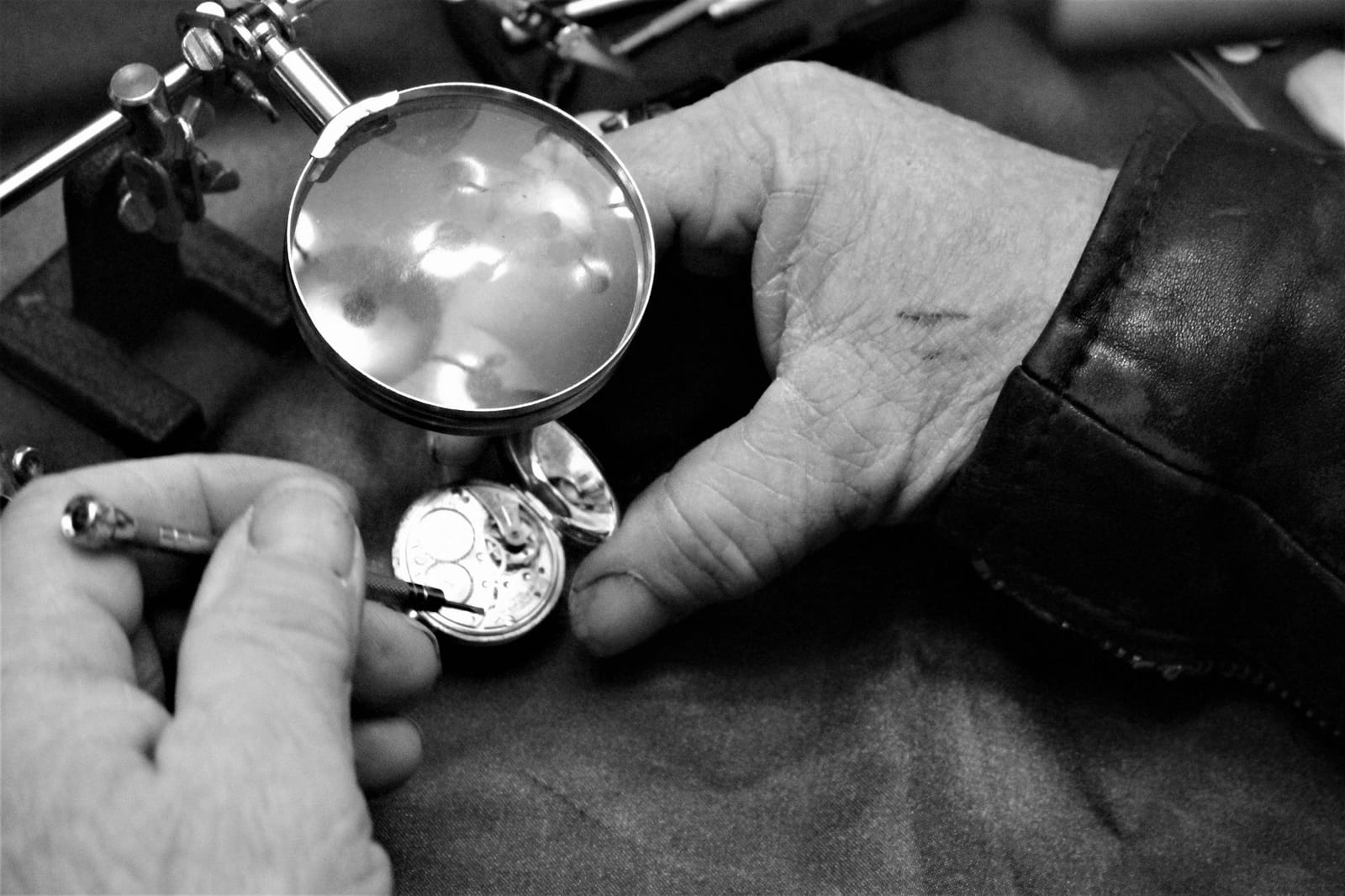 Fotografia in bianco e nero di una lente da orologiaio sopra un movimento da tasca aperto, tenuto in mano